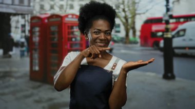 Önlüklü kadın şehir sokaklarında ikonik kırmızı telefon kulübeleriyle Palm 'ı işaret ediyor..