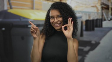 Kadın açık hava geri dönüşüm konteynerlerinin önünde güneşli şehir sokağında el yazısı hazırlıyor. Onaylandı..