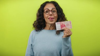 Orta yaşlı bir kadın, canlı sarı bir arkaplan karşısında neşeli bir ifadeyle İzlanda Krona banknotları gösteriyor. Finans ve para kavramını biraz mizahla vurguluyor..
