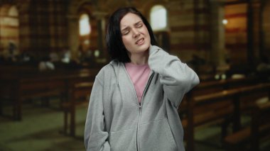 Boyun ağrısı çeken bir kadın loş bir Katolik kilisesinde, ahşap banklarla dikilirken..