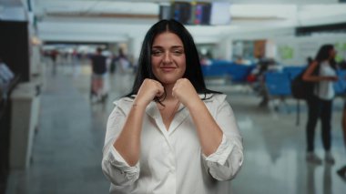 Genç bir kadın havaalanı terminalinde güvenle gölge boksu yapıyor. Geçmişi bulanık. Seyahat bağlamını ve günlük moda tarzını gösteriyor..