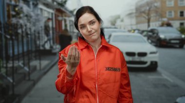 Turuncu hapishane tulumlu kadın jestleri. Arka planda bulanık arabalarla sokakta el ele dolaşır..