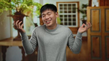 Genç Çinli bir adam, ahşap dekorları ve bitkileriyle sıcak ve davetkar bir atmosfer yaratarak, rahat bir otel odasında duruyor..