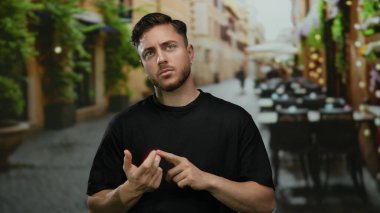 Sakallı genç adam bir şehir restoranının terasında parmaklarını sayıyor. Etrafı bitki ve sandalyelerle çevrili..
