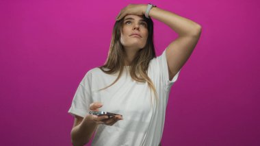 Akıllı telefon kullanan genç bir kadın. Şaşırmış bir ifadeyle canlı pembe izole edilmiş arka plana karşı duruyor.