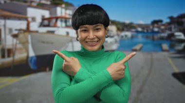 Çinli bir kadın, arka planda kayıklar ve suyla kıyı limanında gülümseyen, açık havada canlı yeşil bir üst giysisi olan zıt yönleri işaret ediyor..