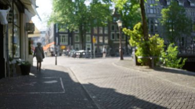 Güneşli gökyüzünün altında kanalın yanında yürüyen bir kadının görüntüsü bulanık. Bokeh etkisi ile cadde boyunca uzanan tarihi mimari ve bereketli ağaçları vurguluyor..