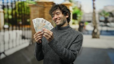 Elinde Czech Koruna banknotları olan bir adam, İspanyol mirasını ve şehir dışı yaşam tarzını gözler önüne seriyor..