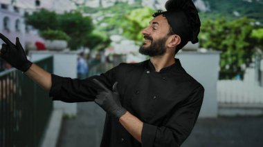 Siyah şef üniformalı İspanyol adam ve sakallı şapkalı mutlu bir şekilde açık hava arka planında, çekici ve davetkar..