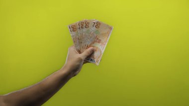 Sarı arka planda el ele tutuşan Türk lirası zenginliği ve finansal başarıyı sembolize ediyor, canlı bir renk arkaplanı ile parasal odağı vurguluyor.