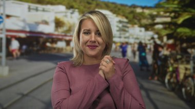 Sarışın kadın hafifçe gülümsüyor ve hareketli bir güneş ışığı sokağında el ele tutuşuyor..