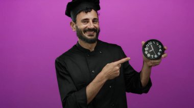Siyah üniformalı İspanyol şef canlı pembe bir arka plan, gösterişli zaman yönetimi ve aşçılık ithafına karşı bir saat tutuyor ve işaret ediyor..