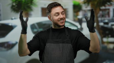Sakallı garson, eldivenli elleriyle büyük bir jest yapıyor. Şehir caddesinde önlük giyiyor. Arka planda da da güvenle gülümseyen bir araba var..