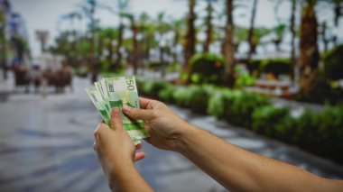 Açık şehir parkında elinde yeşil banknotlar tutan bir adam Norveç parası sergiliyor, parlak bir günde bir iş ya da yatırım temasını yansıtıyor..