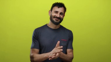 Sakallı İspanyol bir adam canlı sarı bir arka plana el çırpıyor ve gülümsüyor, pozitif duygu ve enerji öneriyor..