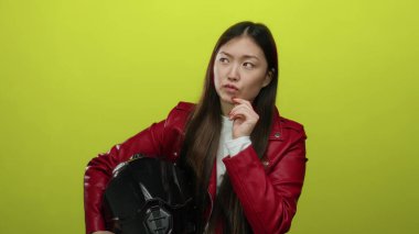 Kırmızı ceketli, parlak sarı arkaplanlı bir kadın düşünceli bir ifade sergiliyor..