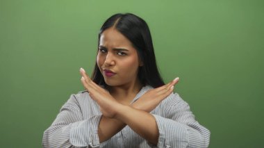 Katı yeşil bir arkaplan önünde kollarını kavuşturarak hayal kırıklığını ifade eden bir kadın, çizgili gömlekle üzgün bir duygu sergiliyor..