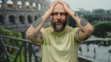 Kel, sakallı, kolları dövmeli bir adam. Roma Kolezyumu 'nun açık havada sıkıntısı var..