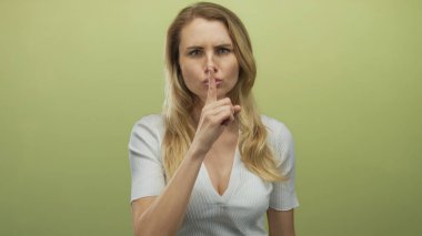 Stüdyoda yakalanan sarı arkaplan karşısında parmakları dudaklarına değen şşşş hareketi yapan kadın, yüzüne odaklanmış bir bakışla sessizlik ya da gizlilik ihtiyacını ima ediyor.