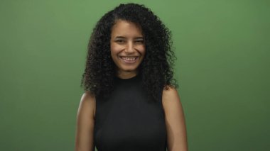 İzole edilmiş yeşil bir arkaplan önünde gülümseyen kadın, enerjik ve minimalist bir ortamda gençlik enerjisi ve pozitiflik sergiliyor..