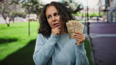 Şehirde orta yaşlı bir kadın elinde Güney Afrika rand banknotlarıyla sokakta düşünceli görünüyor..