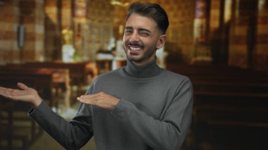 Kilise binasında boyalı camlar arasında başparmak hareketi ve açık avuçlar gösteren İspanyol genç adam; inanç umudu neşe.