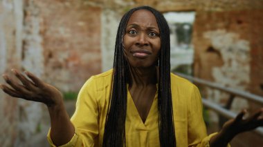 Antik Roma harabelerinde kıvırcık saçlı bir kadın sarı bir gömlek giyerken tarihi bir mekanda düşünceli bir anı yakalıyor..