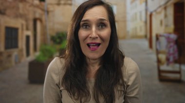 Kadın, eski bir şehir kaldırım taşı sokakta yıpranmış taş duvarlar karşı ellerle yanakları kaplar; şaşkınlık sevinç şaşkınlık sevinç heyecan.