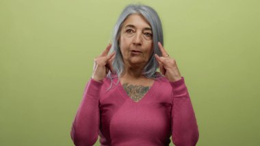 Gri saçlı yaşlı kadın sarı arka plana kaya jesti yapıyor. Cesaret ve kendine güvenini gösteriyor..