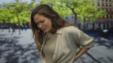 Güneşli yeşil bir parkta sırt ağrısı çeken genç İspanyol kadın, gündüz vakti dışarıda rahatsızlık ve gerginlik yaşıyor..