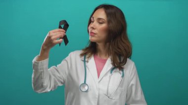 Steteskoplu kadın doktor, izole edilmiş yeşil arka plana karşı siyah kurdele tutuyor ve farkındalığı simgeliyor.