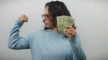 Beyaz bir arkaplan karşısında Arjantin pezosu tutan orta yaşlı bir kadın güçlü bir güç ve finansal güven gösteriyor..