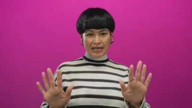 Avuç içleri açık genç Çinli bir kadın soyutlanmış pembe bir arka plana karşı bir jest yapıyor ve bunu onaylamadığını söylüyor.