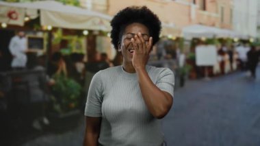 Kalabalık bir şehir caddesinde arka planda canlı teras restoranları olan neşeli şehir manzarası sergileyen bir kadın..