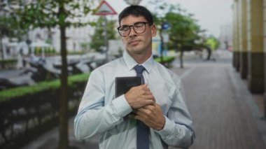 Açık mavi tişörtlü ve kravatlı İspanyol genç adam ağaçlarla kaplı caddede kitaptan sandığa sıkıca tutunuyor..