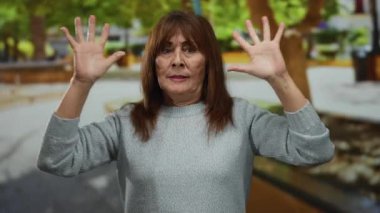 Gri kazaklı İspanyol bir kadın yeşil ağaçlarla çevrili sakin bir parkta gözleri kapalı meditasyon yapıyor..