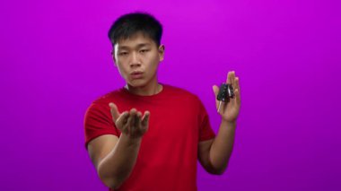 Kırmızı tişörtlü genç Çinli adam elinde araba anahtarlarıyla öpüşüyor. İzole edilmiş pembe arka plana karşı. Sevgi ve ulaşım taşıyor..