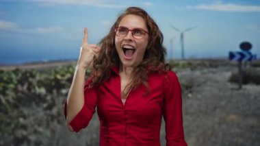 Arka planda yel değirmenleri, kırmızı bir gömlek ve gözlük takan bir kadın, doğanın kucaklamasında neşeli bir anı yakalıyor..