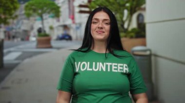 Yeşil gönüllü gömlekli bir kadın şehir caddesinde kendine güvenen farklı yönleri göstererek duruyor. Gencin kendine güveni ve nişanını gösteriyor..