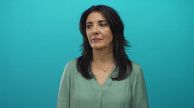 İspanyol orta yaşlı, yeşil bluz ve inci kolye giyen bir kadın gözlerini kapatır ve kafasını turkuaz stüdyo duvarına yaslar; dinginlik iç gözlem meditasyonu.