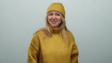 Hardal rengi süveter ve tarafsız bir ifadeyle bereli bir kadın, parlak, minimalist bir ortamda gevşek bir kış havası sergiliyor..