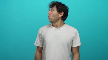 İspanyol adam mavi arka plana şaşırdı, beyaz gömlek giyiyor ve komik ve büyüleyici bir yüz ifadesi sergiliyor..