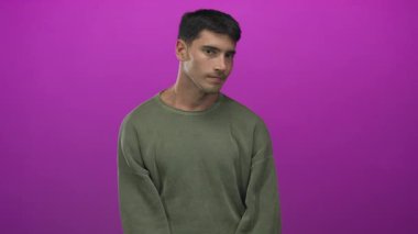 Genç İspanyol adam yeşil kazak giyiyor ve mor stüdyoda parmak uçlarına basıyor..