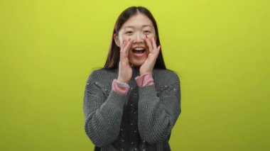 Sarı arka planda gülen, rahat bir süveter giyen, mutluluk ve enerji sergileyen, uzun siyah saçlı, neşeli, izole bir ortamda yaşayan Asyalı bir kadın.