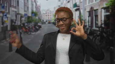 Genç Afro-Amerikalı kadın, güneşli şehir caddesinde bisiklet parkının yanında el işareti yapıyor. Onaylandı..