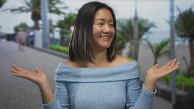 Deniz kenarındaki bir güvertede neşeyle gülümseyen bir kadın, neşeli yüzünü palmiye ağaçları ve mavi gökyüzü ile sergiliyor, dingin çevreyi büyütüyor..