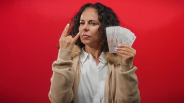 Orta yaşlı bir kadın kırmızı arka planda Singapur dolarlarıyla taş jestler yapıyor..