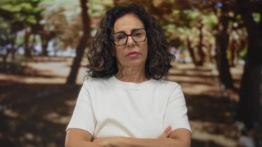 Orta yaşlı İspanyol kadın kolları yeşil parkta meşe ağaçlarının altında çapraz hareket etti; reddedilme ciddiyeti.