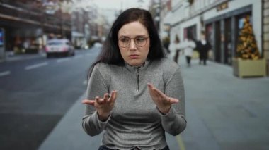 Kadın kışın şehir caddesinde, bulanık yayalar ve şehir dekorasyonlarıyla çevrili, şaşkın bir ifadeyle kendini işaret ediyor..