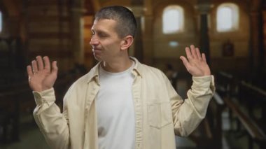 Kilisenin içinde el kol hareketi yapan, dinsel bir ortamda sakinliğini ifade eden bir adam..